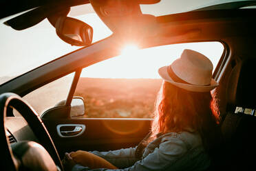 Woman wearing hat sitting in car enjoying sunset - EBBF04064