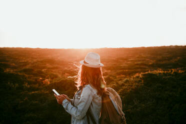 Frau mit Rucksack und Smartphone bei Sonnenuntergang - EBBF04067