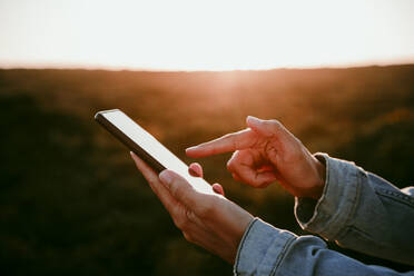 Frau benutzt Mobiltelefon bei Sonnenuntergang - EBBF04068