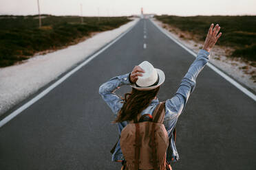 Backpacker with hand raised standing on road - EBBF04070