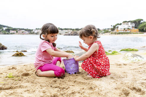 Mädchen geben Sand in einen Eimer am Strand - GEMF04872