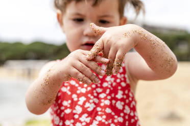 Mädchen schaut auf schmutzige Hände, während sie am Strand steht - GEMF04874