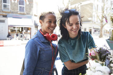 Lächelnde Frauen, die auf dem Markt stehen und Blumen prüfen - PMF01824