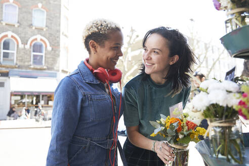 Lächelndes lesbisches Paar, das sich beim Kauf eines Blumenstraußes auf dem Markt gegenseitig anschaut - PMF01826