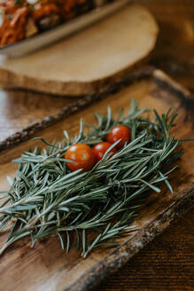 From above of whole ripe cherry tomatoes on fresh rosemary sprigs with pleasant scent on wooden plate - ADSF24917