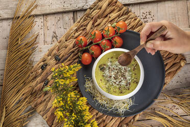 Overhead view of crop anonymous chef with bowl of yummy vegetarian cream soup with crushed pistachios and condiments on top - ADSF24985