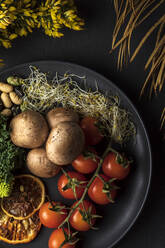 Draufsicht auf Teller mit Bündel frischer Kirschtomaten neben gekochten Kartoffeln und Sprossen auf grauem Hintergrund mit Blumen - ADSF24989