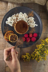 From above of crop anonymous cook with plate of yummy baked flan with ripe raspberries and cinnamon powder - ADSF24992