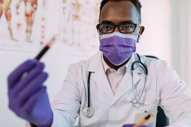 Männlicher afroamerikanischer Arzt in medizinischem Handschuh demonstriert Reagenzglas mit Blutprobe auf weißem Hintergrund - ADSF25014