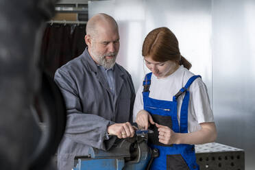 Mature instructor assisting female apprentice working in workshop - LBF03522