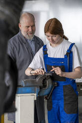 Female apprentice working with machinery while male instructor assisting in workshop - LBF03523