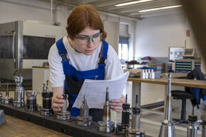 Technikerin bei der Arbeit mit metallischen Maschinenteilen, während sie in der Werkstatt ein Buch liest - LBF03526
