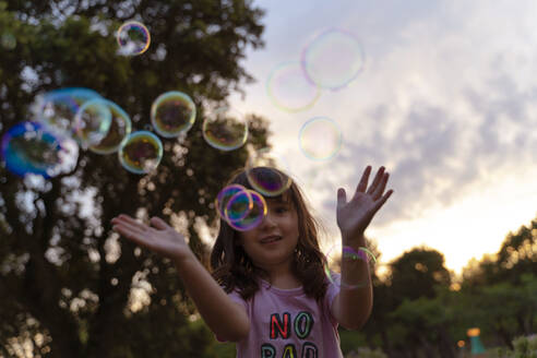 Girl playing with soap bubbles during sunset - GEMF04875