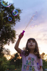 Girl with bubble wand looking up while playing outdoors during sunset - GEMF04878