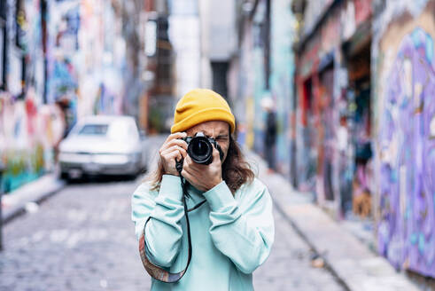 Junger Hipster mit Strickmütze, der eine Graffiti-Wand mit der Kamera in der Stadt fotografiert - ADSF25081