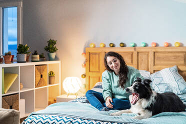 Young woman in glasses sitting on bed with border collie dog - ADSF25141