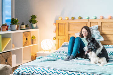 Junge Frau mit Brille sitzt mit Border Collie Hund auf dem Bett - ADSF25142