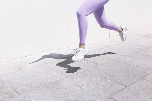 Weibliche Athletin beim Joggen auf dem Fußweg an einem sonnigen Tag - EGHF00019