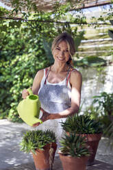 Smiling mature woman watering plants while standing in garden - VEGF04637