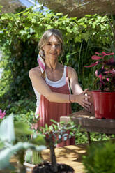 Smiling woman keeping potted plant while standing at backyard - VEGF04651