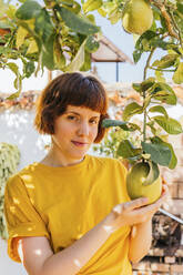 Beautiful woman touching lemon fruit in home garden - MGRF00282