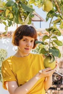 Schöne Frau berührt Zitronenfrüchte im heimischen Garten - MGRF00282