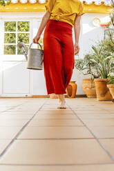 Woman with watering can walking at home garden - MGRF00293