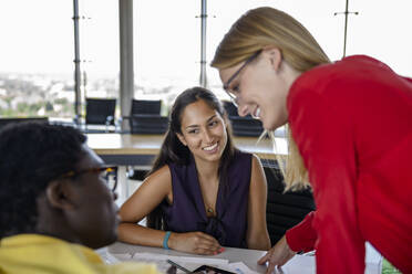 Lächelnde Geschäftsfrauen, die einen männlichen Kollegen ansehen, während sie bei einer Besprechung im Büro diskutieren - BMOF00837