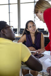 Male and female colleagues looking at businesswoman explaining over digital tablet at office - BMOF00838