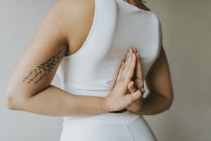 Tattooed yoga teacher with hands clasped behind back exercising at health club - OCAF00664