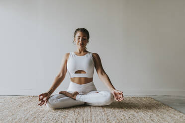 Weiblicher Fitnesslehrer meditiert im Lotussitz im Yogastudio - OCAF00670