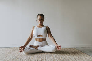 Female fitness teacher meditating in lotus position at yoga studio - OCAF00670