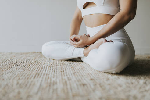 Yogalehrer beim Meditieren im Schneidersitz auf einem Teppich im Fitnessstudio - OCAF00673