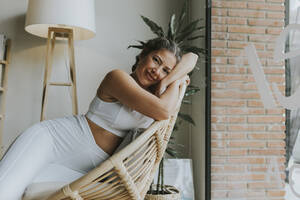 Smiling woman relaxing on chair at yoga studio - OCAF00676