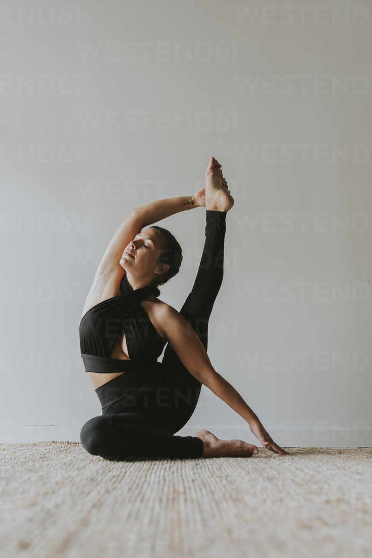 Flexible female yoga instructor with eyes closed exercising at