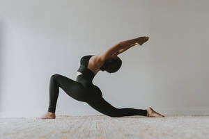 Female fitness teacher with arms raised bending backwards while practicing yoga - OCAF00683