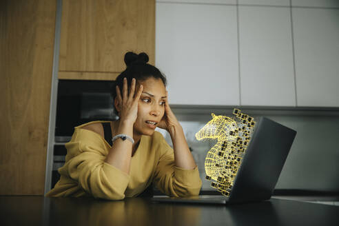 Woman with head in hands looking at Trojan virus icon on laptop - LIFIF00048