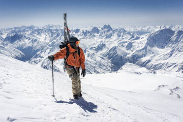 Mann mit Skistock und Splitboard beim Besteigen eines schneebedeckten Berges im Urlaub - CAVF94221
