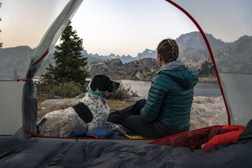 Woman sitting with dog by tent while camping during vacation - CAVF94223