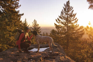 Side view of young woman hiking with dog on mountain during sunset - CAVF94229