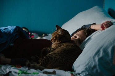 Boy Lays In Bed Awake While His Tabby Cat Snuggles Up Against His Face - CAVF94249