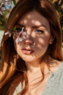 Portrait of a young blue-eyed woman surrounded by almond blossoms - CAVF94269