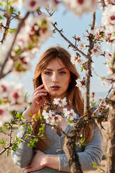 Portrait of a young blue-eyed woman surrounded by almond blossoms - CAVF94270