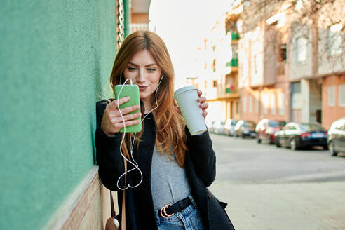 Geschäftsfrau hält eine Kaffeetasse, während sie auf ihr Telefon schaut - CAVF94272
