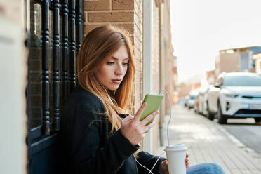 Eine blonde Geschäftsfrau trinkt Kaffee und schaut auf ihr Handy - CAVF94276