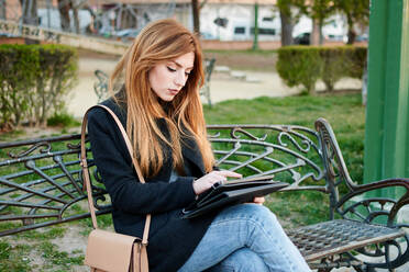 Eine attraktive junge Frau schaut in einem Park auf ihr Tablet - CAVF94285