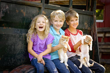 Drei glückliche blonde Kinder spielen mit Kätzchen im Freien. - CAVF94294