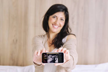 Lächelnde schwangere Frau zeigt Ultraschall auf dem Mobiltelefon - AODF00508