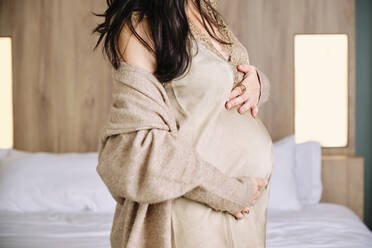 Schwangere Mutter mit Händen auf dem Bauch im Schlafzimmer zu Hause - AODF00512