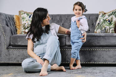 Lächelnde schwangere Frau mit süßer Tochter im Wohnzimmer zu Hause - AODF00533